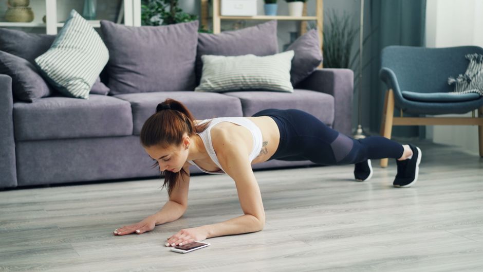 Femme en position de planche sur un tapis de sport dans un salon, séance abdos à la maison
