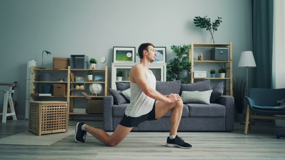 Fente basse sur tapis dans un salon : genou arrière au sol, jambe avant pliée, buste droit