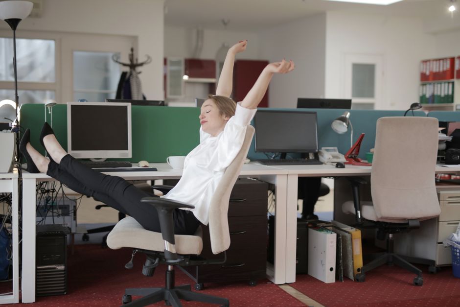 Personne assise à un bureau qui s'étire les bras au-dessus de la tête devant son écran