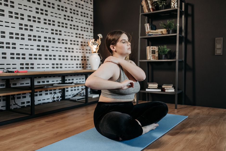 Femme assise en tailleur sur un tapis de sport dans un salon, en plein exercice de respiration hypopressive