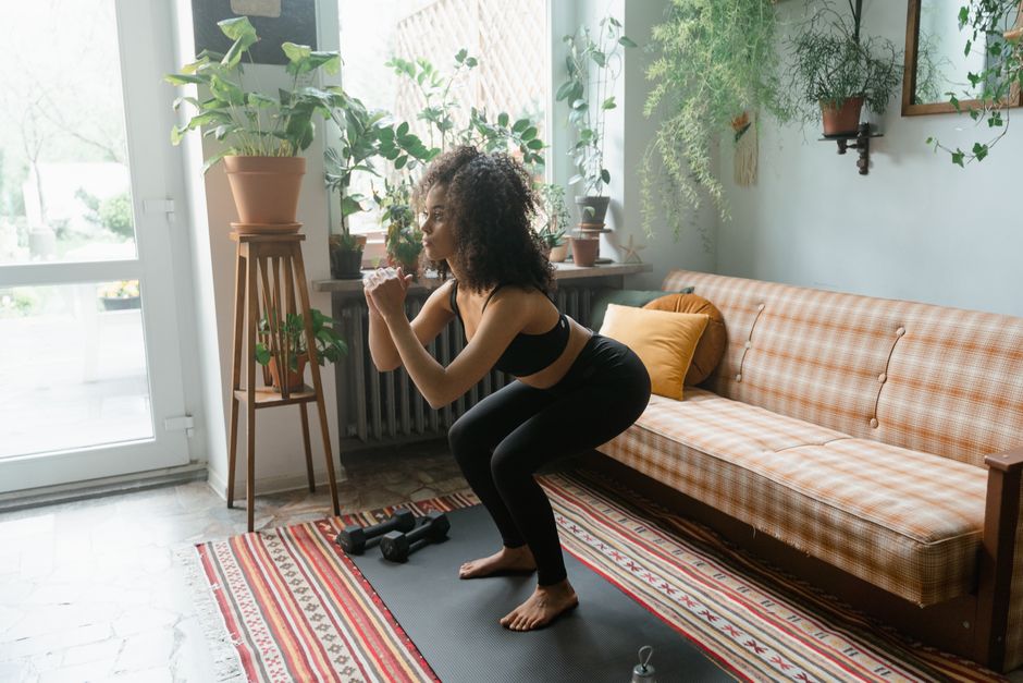 Femme réalisant un squat jump dans son salon, réception genoux fléchis