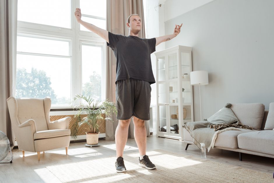 Homme debout dans un salon, talon ramené vers la fesse pour étirer le quadriceps